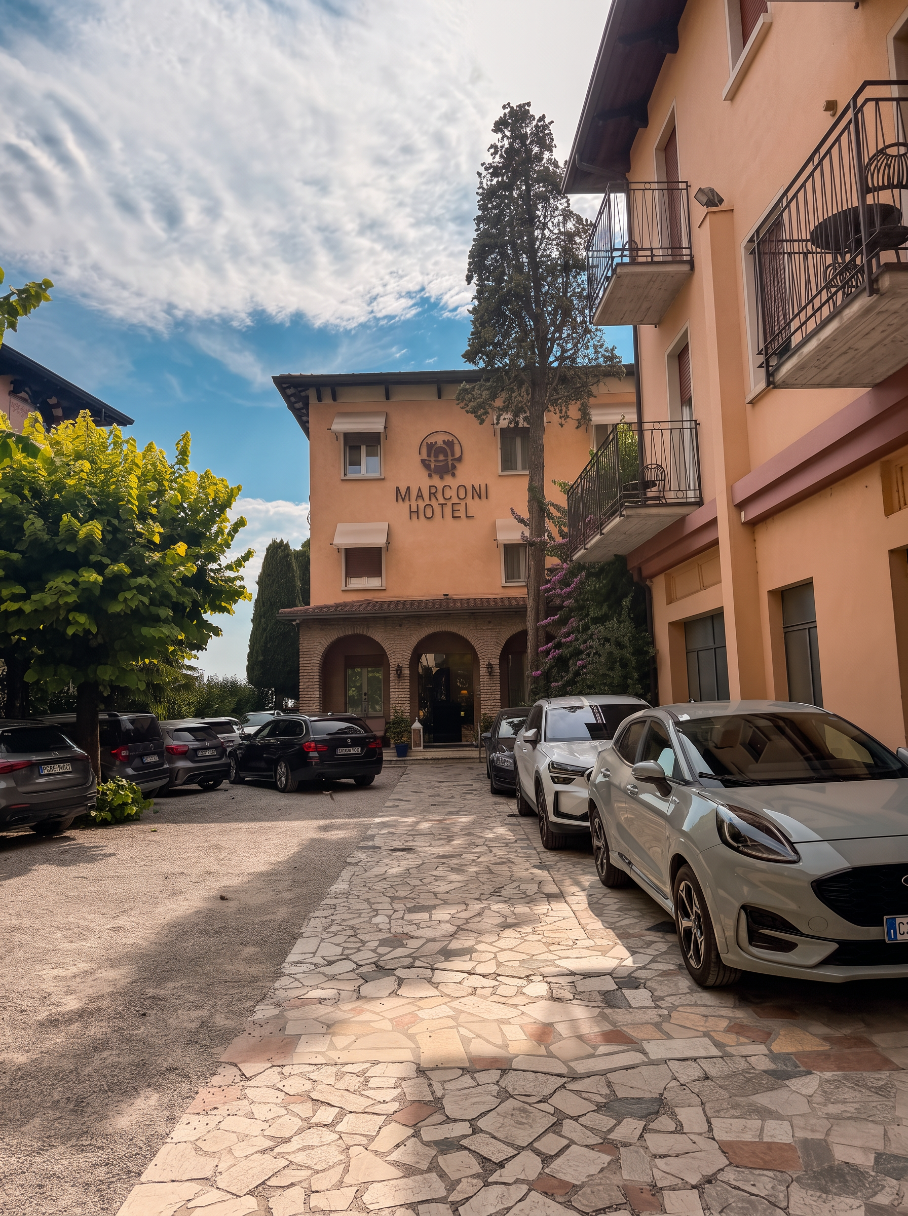 Hotel Marconi in Sirmione, Lake Garda, with its peach-coloured facade, arched entrance and tree-lined driveway on a sunny day